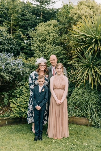 A husband, wife and their two children are stood outside. They are dressed for a wedding.