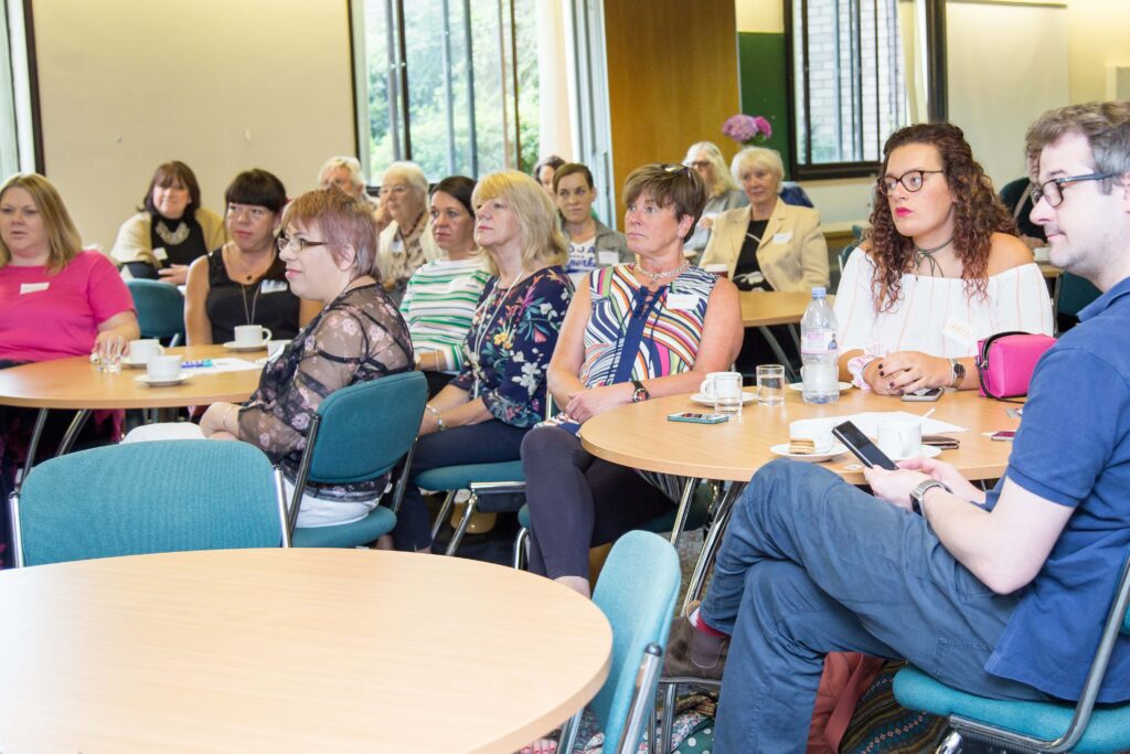 A group of people sat round tables listening to a talk.