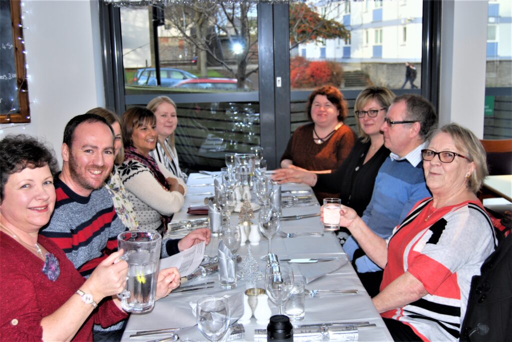 Nine people sitting at a restaurant table, smiling into the camera.