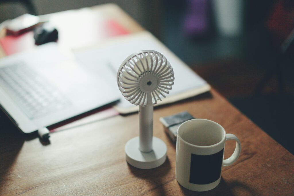 a small fan on a desk, next to a mug
