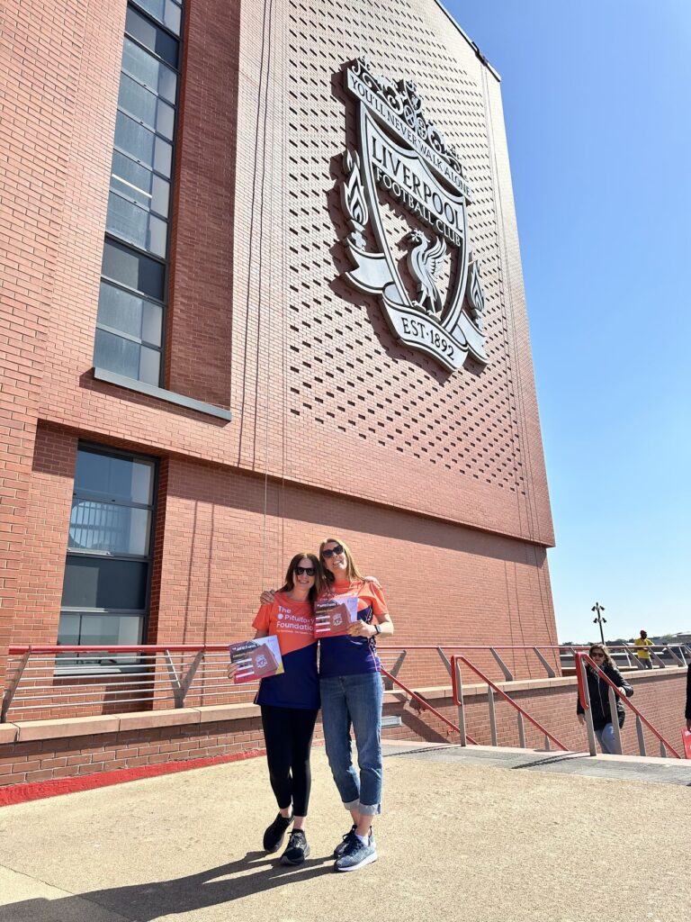 Roz and her friend are stood in front of Anfield stadium holding certificates. They are smiling and have just completed the Anfield Abseil fundraising event.