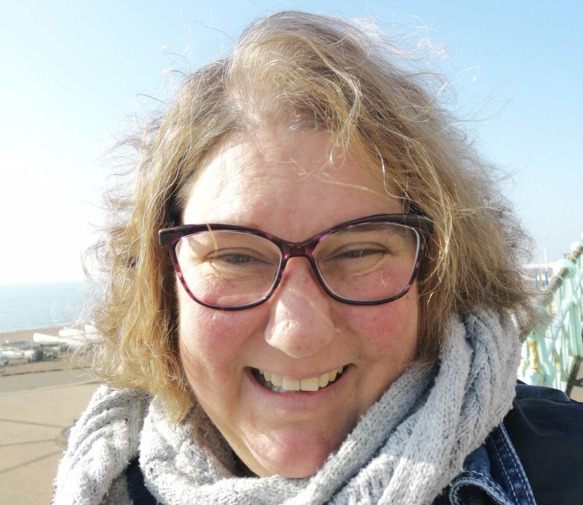 A woman outside on a sunny day, wearing glasses and a scarf