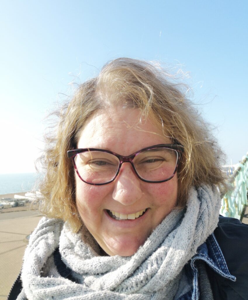A woman outside on a sunny day, wearing glasses and a scarf