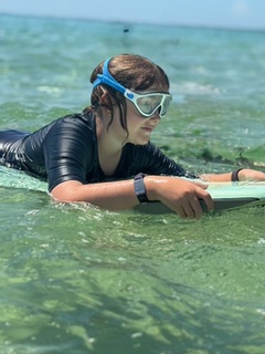 A young girl is in the ocean on a body board. She is wearing scuba goggles 