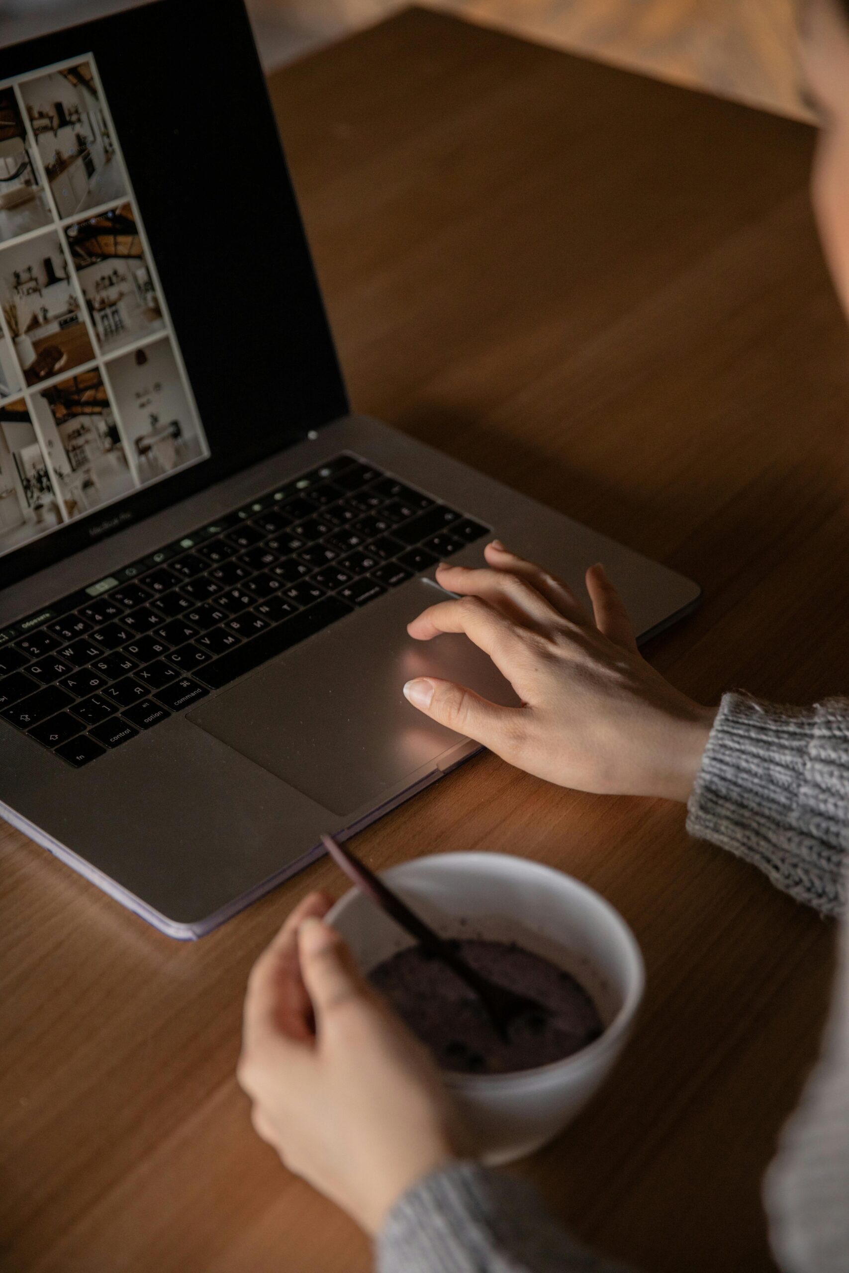 A laptop placed on a table, with a person's hand on the mouse pad. The person is also holding a cup of tea in their other hand