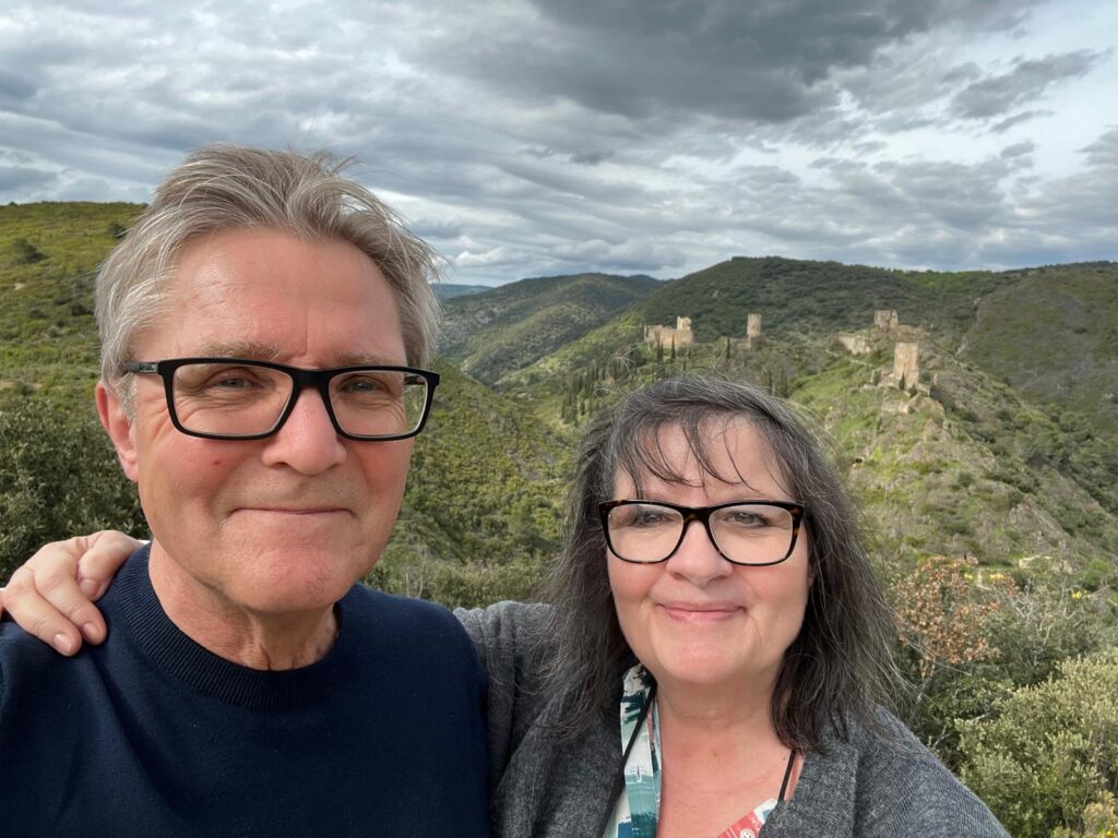A man and woman are stood together at the top of a hill. There is a green lanscape behind them and a cloudy sky