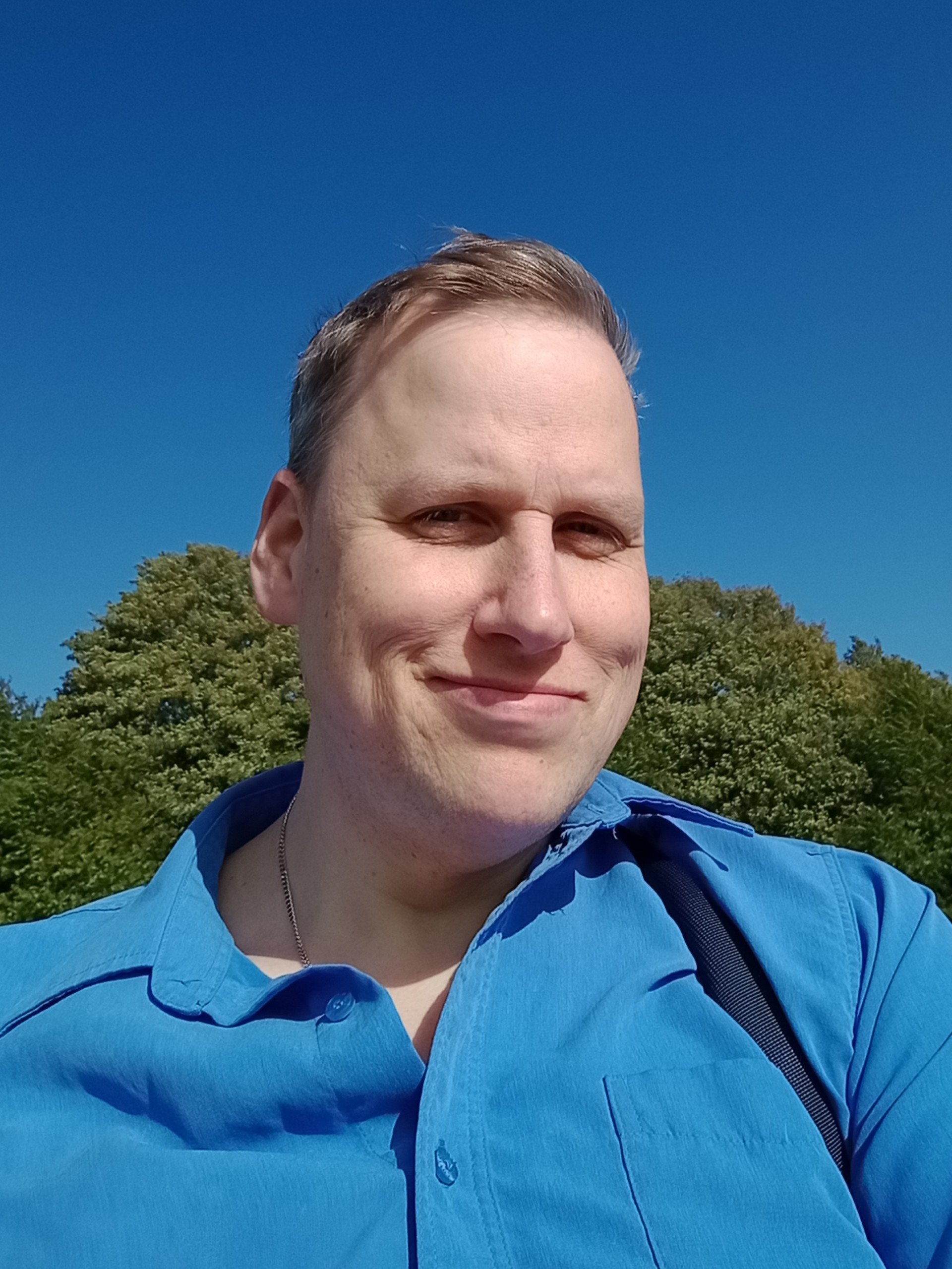 A man in a blue shirt is smiling in the sun