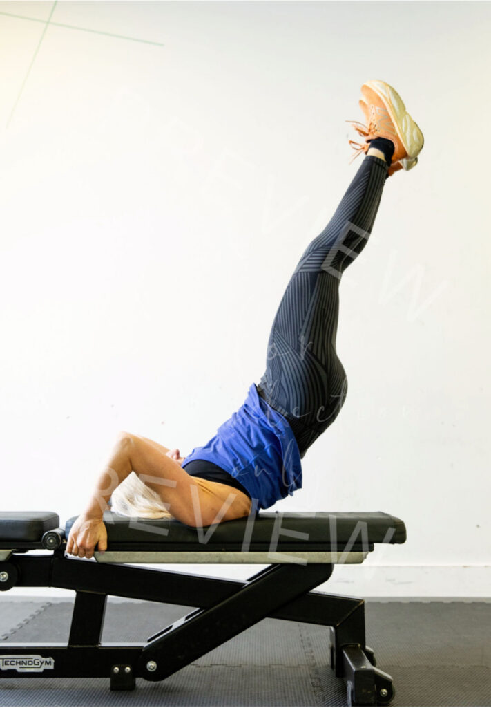 A woman is balancing on a gym bench, holding her legs up in the air