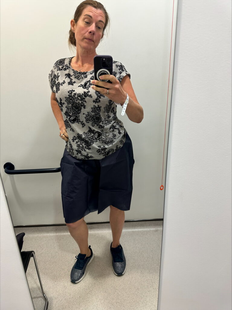 A woman in a hospital bathroom wearing the navy paper shorts that people are given before a colonoscopy.