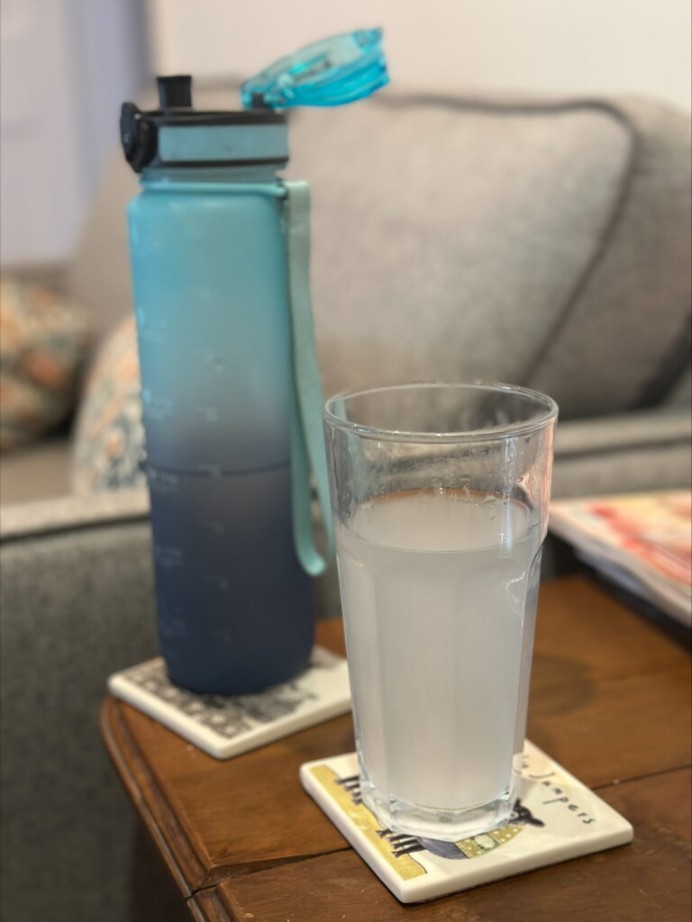 A large bottle of water and a glass of clear liquid on a table. the glass contains the bowel prep drink given before a colonoscopy