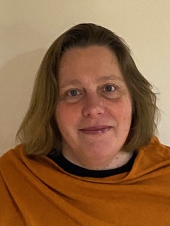 A woman with short brown hair stood against a white wall