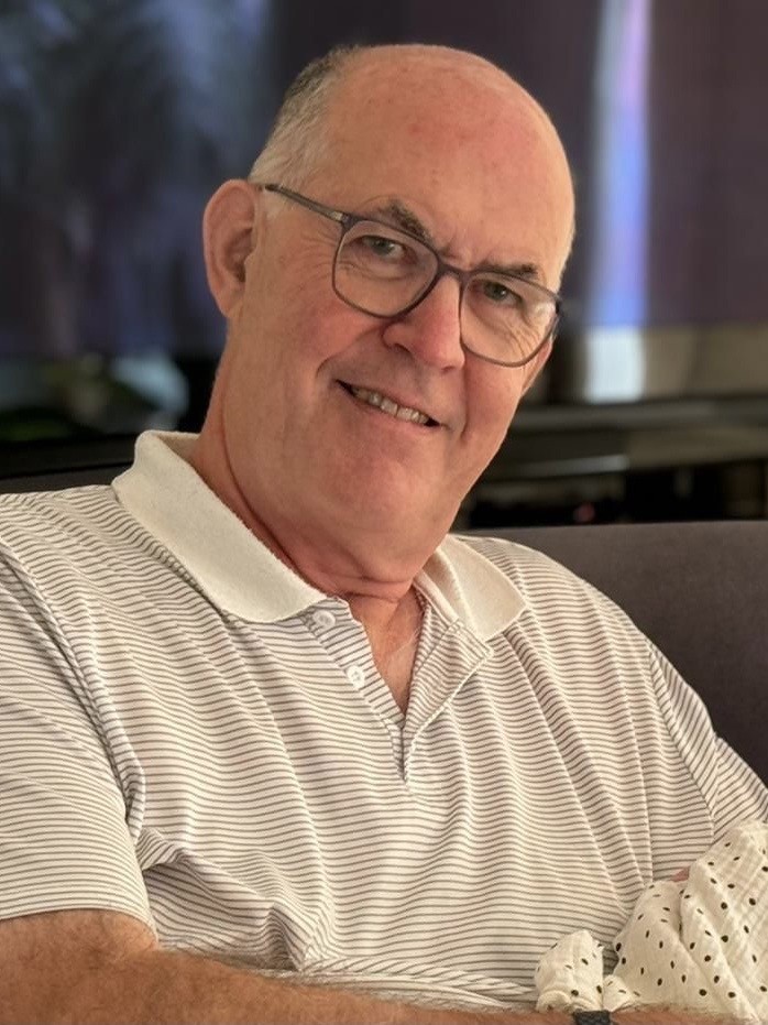 A man wearing glass and a white polo shirt smiles at the camera