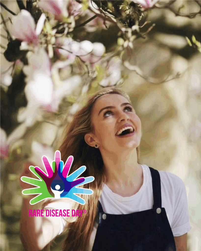 Tilly Rose smiling under a tree with pink flowers, with the Rare Disease Day logo at the bottom left of the picture