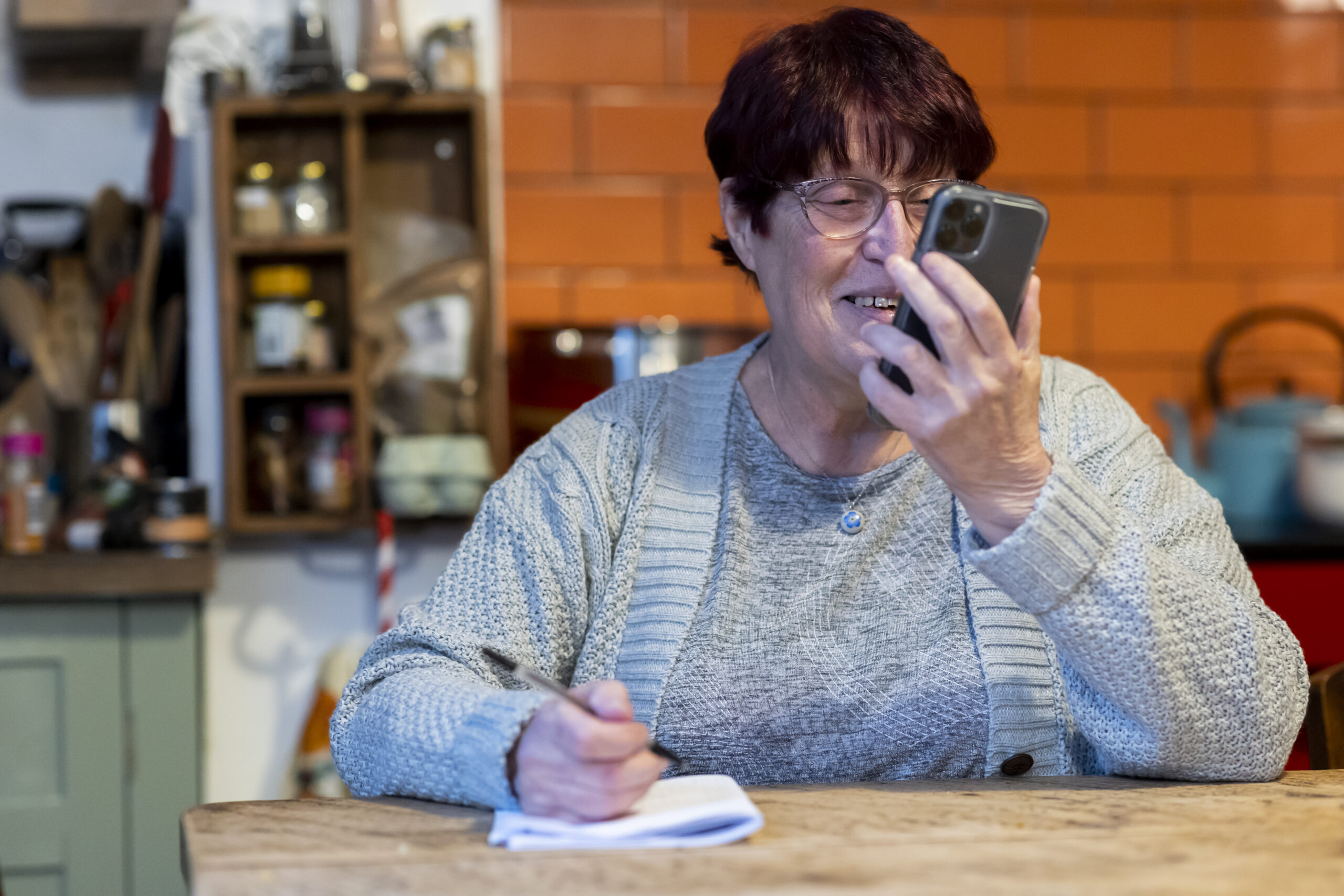 A woman watching a video on her phone and taking notes