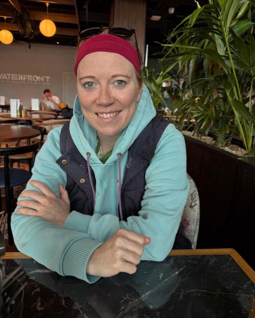 Helen smiling sitting at a table indoors wearing a hat
